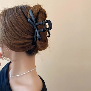 Detail of elegant black 3D bow hair claw clip styled on a woman's hair with pearl necklace