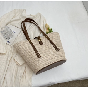 Flat lay of woven beige tote bag with brown PU leather trim and buckle on white linen