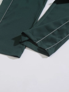 Macro detail of dark green woven trousers featuring grey reflective side stripes and stitching