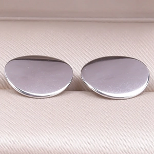 Macro detail of silver minimalist round stud earrings on champagne fabric surface