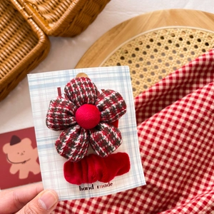 Detail of handmade red and green plaid fabric flower hair clip with a bow on display card
