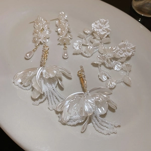 Detail showing elegant pearl flower earrings with tassels and crystal accents on ceramic tray