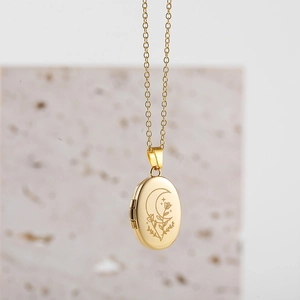 Detailed close-up of oval gold locket necklace with moon and botanical engravings