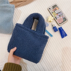 Mini sac à main bleu marine en sherpa duveteux tenu au-dessus d'une surface blanche