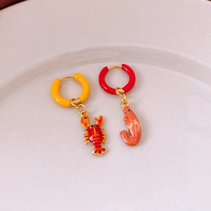 Macro shot of asymmetric shrimp and lobster enamel earrings on a white ceramic plate