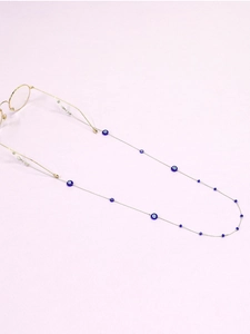 Detail of blue evil eye beads on a golden metal chain for eyewear on lavender background