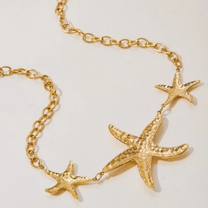 Detail von drei goldenen Seestern-Anhängern an einer runden Gliederkette im Vintage-Look