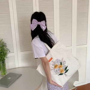 Detail of floral embroidery on a beige canvas tote bag with a purple satin bow clip