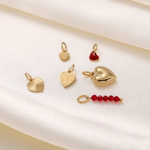 Detail of assorted gold and red enamel heart pendants on a soft white silk background