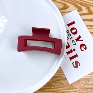 Macro shot of burgundy matte rectangular claw clip on a white plate with soft lighting