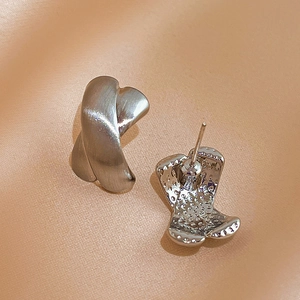 Macro shot of silver X-shaped cross earrings showing brushed texture and butterfly clasp
