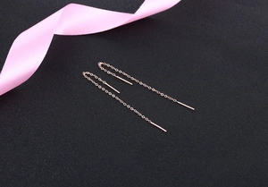 Detailed macro view of long rose gold tassel earrings with fine chain on black texture