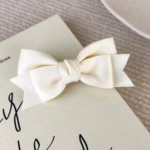 Detailed view of a cream white ribbed satin bow hair clip on a vintage book page