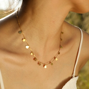 Dettaglio di una collana dorata con ciondoli a stella e cuore sulla clavicola