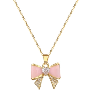 Macro detail of gold bow pendant with pink enamel and sparkling heart-shaped zircon