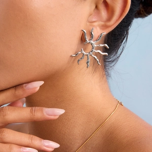 Detailed view of a silver sunburst earring with fluid texture worn by a model