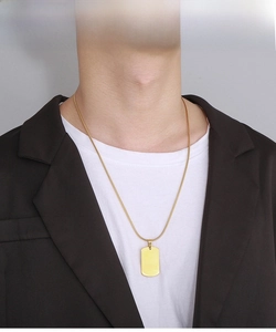 Polished gold dog tag pendant on snake chain necklace worn by a model in close-up shot