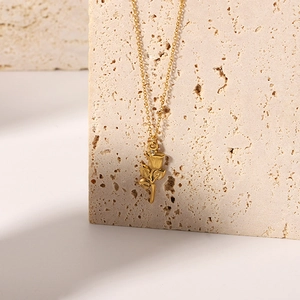 Close-up of 18K gold-plated 3D rose flower pendant with a fine cross chain on stone