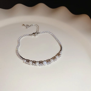 Close-up of silver chain bracelet featuring pearls and clear zircons on a ceramic tray