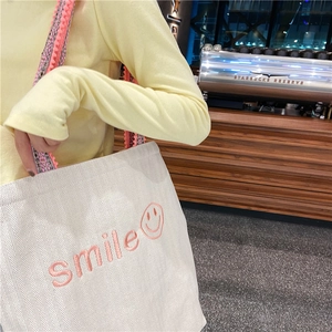 Detail of white canvas tote bag featuring pink smile embroidery and colorful tassel strap