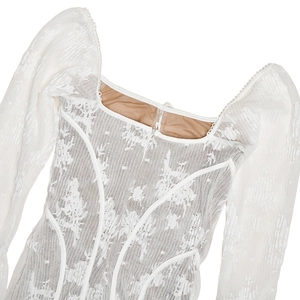 Close-up of white lace fabric with square neckline and intricate stitching details