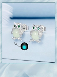 Macro detail of S925 silver owl stud earring with glowing stone and green zircon eyes