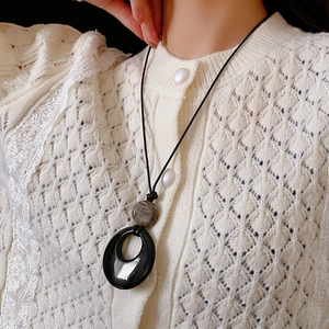 Dettaglio della collana con ciondolo geometrico in agata e perlina grigia su cardigan
