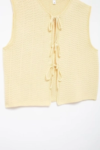 Detail of light yellow knit vest showing texture, bow ties, and size S neck label