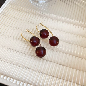 Minimalist dark red resin cherry earrings with golden stems on textured glass plate