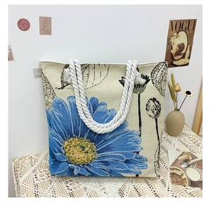 Close-up of beige canvas tote with blue daisy embroidery and woven rope handles