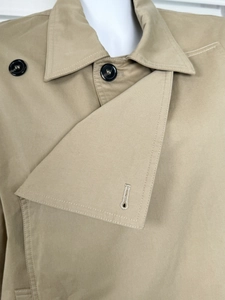 Detail of khaki trench coat collar featuring black resin buttons and twill fabric texture