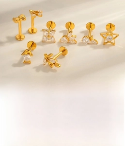 Macro shot of 1.2mm titanium bow and fish ear studs with cubic zirconia in gold