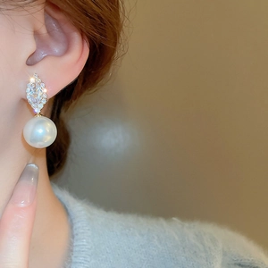 Macro detail of geometric gold earrings with cubic zirconia and round white pearl drops