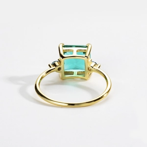 Detail showing high-quality emerald cut green gemstone with blue side stones in gold setting