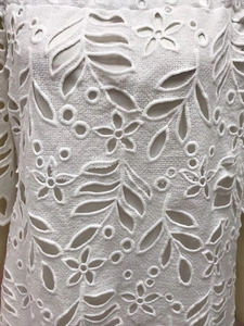 Nahaufnahme von weißem Spitzenstoff mit filigranem Hohlmuster und floralen Stickereidetails