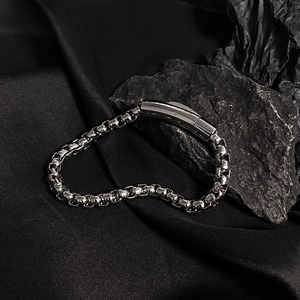 Macro shot of a silver titanium steel chain bracelet with a smooth clasp on a dark stone