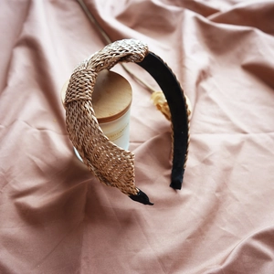Close-up of beige raffia woven headband with black lining on soft fabric background