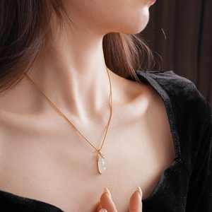 Macro shot of gold-plated eggplant pendant necklace with white chalcedony on neck