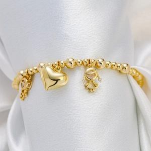 Gold beaded bracelet with heart and girl charms on white silk background