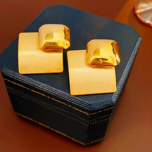 Macro detail of layered gold rhombus earrings on a premium navy textured jewelry box