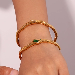 Detailed shot of 18K gold plated wavy bracelets with emerald and white zircon accents