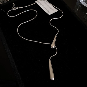 Detailed close-up of double teardrop pendants on silver snake chain over black velvet background