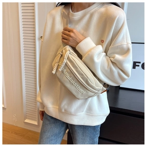 Close-up of cream canvas chest bag featuring adjustable strap and letter print detail
