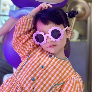 Cute pink flower-shaped sunglasses for kids worn by a girl in a checkered orange dress