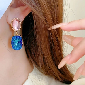 Macro detail of vintage gold earrings with pink oval gem and blue rectangular crystal drop