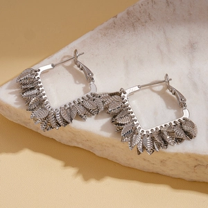 Détail de créoles carrées avec pendentifs feuilles sur fond en marbre élégant
