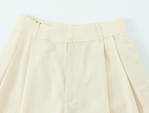 Détail d'un pantalon crème à taille haute montrant les plis et la texture du tissu tissé