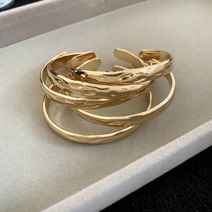 Close-up of stacked golden bracelets with hammered texture on a gray velvet tray