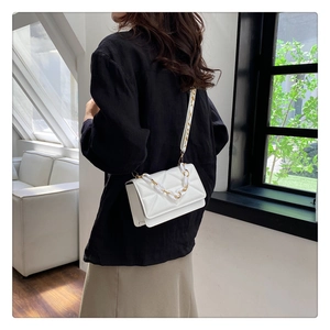 Detailed shot of white quilted crossbody bag with gold-tone chain and patterned strap