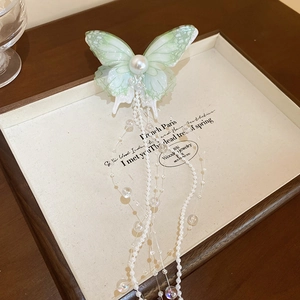 Detail of light green butterfly hair clip featuring a large pearl and long beaded tassels
